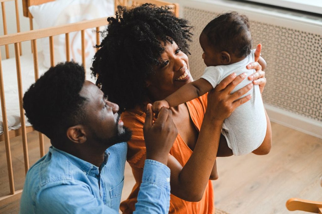parents-carrying-a-baby-11369182 African American parents lovingly interacting with their baby indoors, showcasing family love and joy.