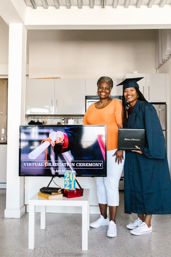 woman-and-her-daughter-in-graduation-gown-smiling-and-posing-for-the-photo-7713405 A proud family celebrating a virtual graduation ceremony at home with smiles and warmth.